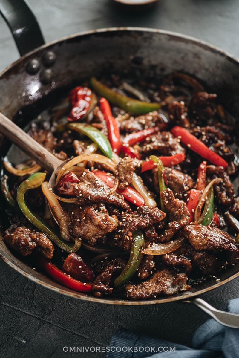 Easy Szechuan Beef Stir Fry - Tender crispy beef cooked in a bold sweet sour spicy sauce with peppers and onions. Learn how to make the richest sauce and create crispy beef without deep-frying. {Gluten-free adaptable} Szechuan beef stir fry served in a plate with rice