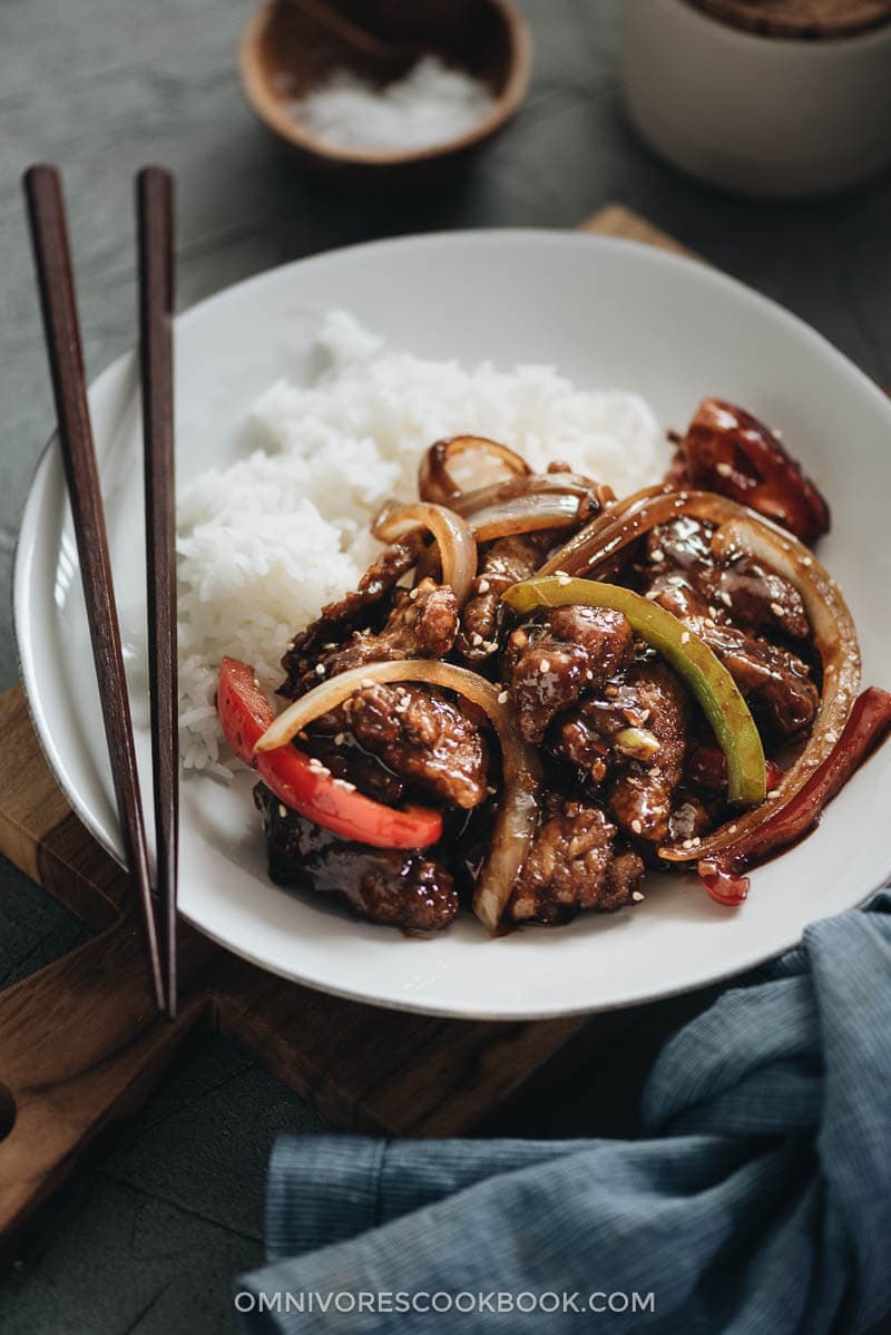 Easy Szechuan Beef Stir Fry - Tender crispy beef cooked in a bold sweet sour spicy sauce with peppers and onions. Learn how to make the richest sauce and create crispy beef without deep-frying. {Gluten-free adaptable} Szechuan beef stir fry served in a plate with rice
