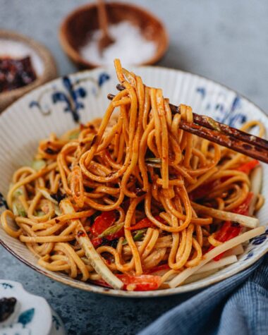Using chopsticks to stretch peanut noodles from a bowl